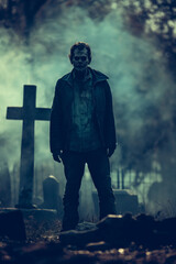 Fototapeta premium Male zombie standing in eerie graveyard at night with fog and tombstones, ideal for Halloween and horror visuals.