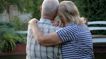 Support relatives and close people in old age alone. Elderly woman puts helping hand on her husband shoulder, caring and soothing nerve pain. Standing still in park, back view. Loneliness in old age