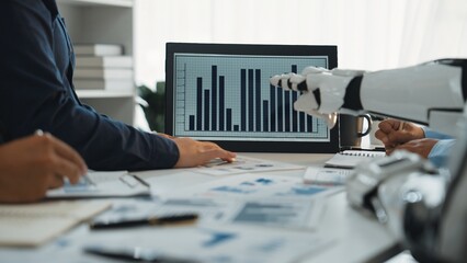A modern workspace showcasing human collaboration with a robot in the process of data analysis, featuring a digital screen displaying statistical graphs.Noogenesis