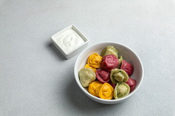 Multicolored dumplings in a bowl with sour cream.