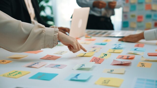 A group of professionals engages in a collaborative brainstorming session, using colorful sticky notes for idea generation and strategy planning at a modern office desk. SACTR