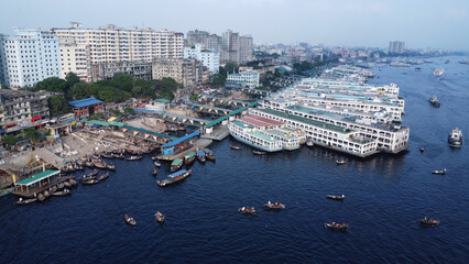 Dhaka is located on the banks of the Buriganga river. Aerial view of Sadar Ghat and the Buriganga river with modern cityscape and boats, Dhaka, Bangladesh.