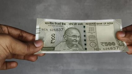 Hand checking five hundred rupee indian currency note money for analyzing authenticity due to suspicion of forgery or counterfeit. India fake money concept. Extreme closeup macro side view.