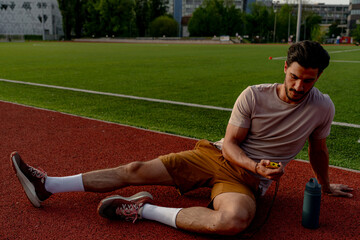 Young sportsman resting on a running track and checking his performance on a stopwatch after a...