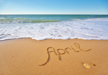 April word written on sea sand shore beach at day.