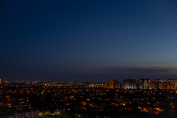 Cityscape with illuminated residential buildings and glowing street lights under deep blue evening sky. Urban skyline at twilight. Nighttime city and modern architecture concept.