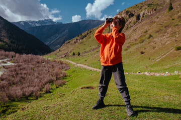 Fototapeta premium Child tourist with binoculars standing in high mountains on summer day
