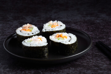 Four sushi rolls on a black plate. The rolls are made of seaweed and rice. The plate is placed on a dark surface