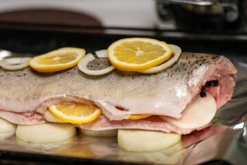 Raw gutted red fish with onion rings and lemon slices, prepared for cooking with fresh and vibrant ingredients