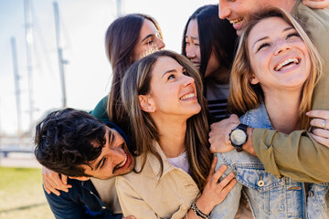 Obraz premium Diverse group of young adult friends having fun hugging each other outside. Joyful millennial people laughing enjoying time together. Community and friendship concept