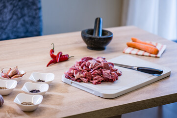 Raw beef meat chopped in cubes with knife, carrots, chili pepper and spices on cutting board. Cook recipe step-by-step. Pilaf recipe in pictures.