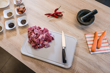 Raw beef meat chopped in cubes with knife, carrots, chili pepper and spices on cutting board. Cook recipe step-by-step. Pilaf recipe in pictures.