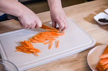 Female hands cut carrot on a cutting board for pilaf into strips. Cooking in the kitchen. Pilaf recipe in pictures. Cooking step.
