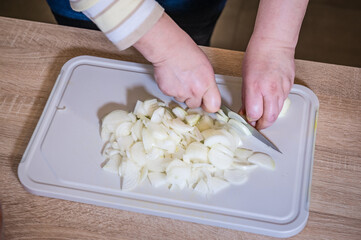 Women's hands chopping onions on a chopping board for pilaf. Cooking in the kitchen. Cook recipe...