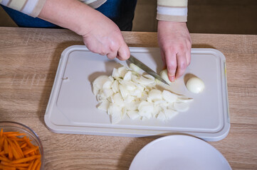 Women's hands chopping onions on a chopping board for pilaf. Cooking in the kitchen. Cook recipe step-by-step. Pilaf recipe in pictures.