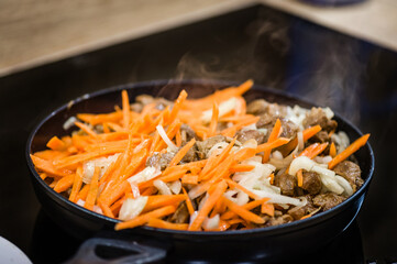 A frying pan on an induction cooker preparing carrots, meat and onions.  Cook recipe step-by-step. Pilaf recipe in pictures.