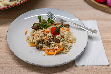 On the serving table, the pilaf is served in a plate decorated with a tomato. The concept of oriental cuisine.