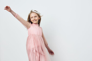 Joyful young girl in a pink dress dances against a minimalistic background, expressing happiness...