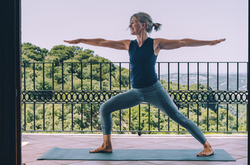 Joyful woman practising warrior II yoga pose on a scenic terrace
