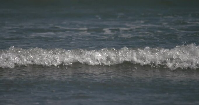 Small ocean waves crests and bubbles as it reaches shore slow motion