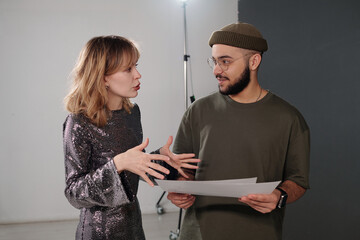 Waist up portrait of young production director talking to smiling actress backstage and holding...