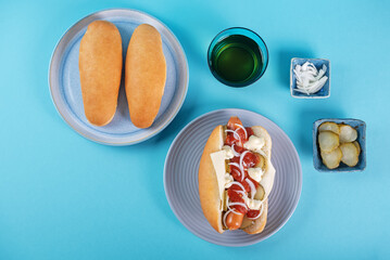 Pickled cucumbers fresh onion frankfurter sausage hot dog sandwich on a blue background