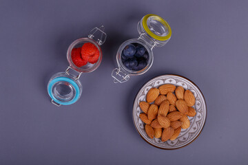 Three jars of colorful fruits and a bowl of almonds on gray.