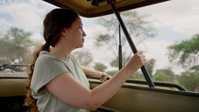 Female tourist in Africa standing in safari game viewer vehicle looking outside. Young woman enjoying wildlife and nature trip vacation in Tanzania Tarangire national park tour. Bumpy road open roof