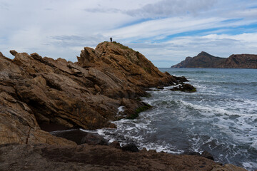 Texturas de la costa rocosa con aguas  cristalinas en la playa de arena negra de Portmán, Murcia