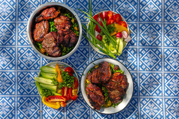 Grilled Meat and Fresh Vegetables on Outdoor Picnic Table. Top view of grilled meat and colorful fresh vegetables served on a patterned blue tablecloth.