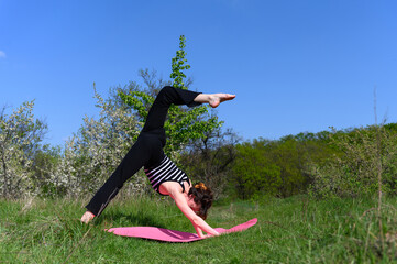 Woman practicing three-legged downward dog pose outdoors in spring garden.