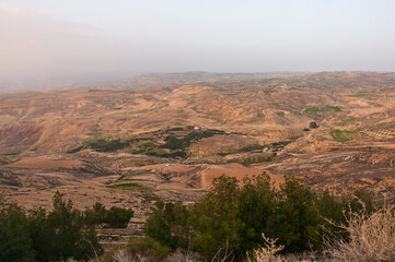 A desert landscape with a few trees and a house in the distance