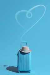 A blue suitcase with a hat on top, an airplane trail in the shape of a heart above it. 