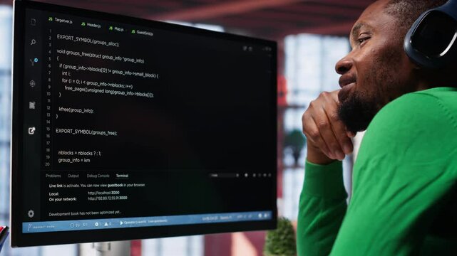 Young IT engineer typing code on computer and running script, programming language. African american technician in modern loft fixing errors within the software, implementing features. Camera A.