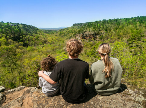 Young diverse family sitting on a rock cliff overlooking a beautiful mountain canyon in the Ozark mountain range in Arkansas
