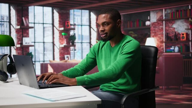 Black man doing remote work feeling uneasy and anxious at desk, shaking his legs and being jittery due to task completion and deadline. Freelancer working under pressure, anxiety. Camera B.