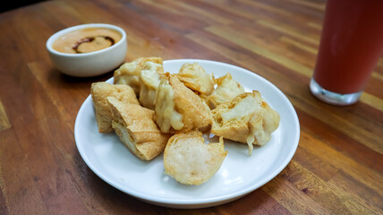 A plate of Indonesian fried tofu stuffed with savory fish cake, served on a white plate over a wooden table