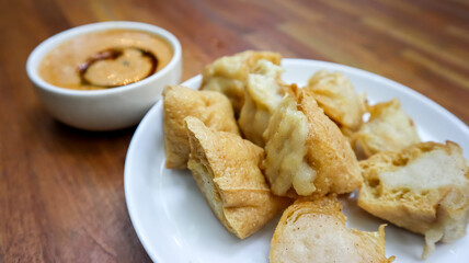 A plate of Indonesian fried tofu stuffed with savory fish cake, served on a white plate over a wooden table