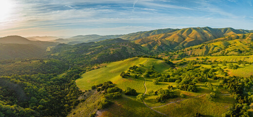 Panoramic drone aerial view of length of Carmel Valley at sunset. Green rolling hills with golden glow. 