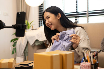 A woman is holding two boxes and smiling. She is sitting in front of a laptop. The boxes are brown and appear to be gifts. The woman seems happy and excited about the boxes
