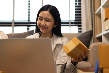 A woman is holding two boxes and smiling. She is sitting in front of a laptop. The boxes are brown and appear to be gifts. The woman seems happy and excited about the boxes
