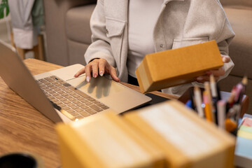 A woman is holding two boxes and smiling. She is sitting in front of a laptop. The boxes are brown and appear to be gifts. The woman seems happy and excited about the boxes

