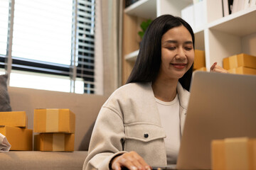 A woman is holding two boxes and smiling. She is sitting in front of a laptop. The boxes are brown and appear to be gifts. The woman seems happy and excited about the boxes
