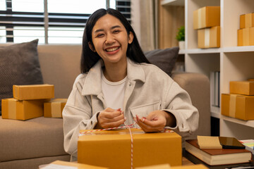 A woman is holding two boxes and smiling. She is sitting in front of a laptop. The boxes are brown and appear to be gifts. The woman seems happy and excited about the boxes
