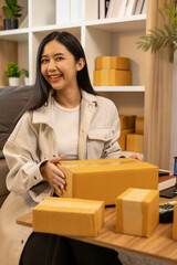 A woman is holding two boxes and smiling. She is sitting in front of a laptop. The boxes are brown and appear to be gifts. The woman seems happy and excited about the boxes
