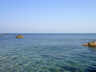Calm clear blue sea and cloudless sky. Rocky bottom is visible through transparent water. Large stones above water surface