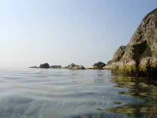 Hot, windless weather at sea. Sky and water almost merge. A small group of low rocks separates the...