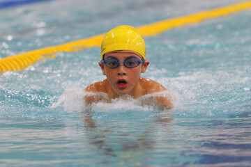 Focused young boy swimming in pool wearing yellow cap and blue goggles during competition