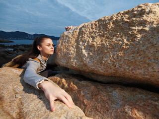Young woman climbing rocky terrain, expressing determination and strength, wearing casual outdoor clothing, against a scenic backdrop, suitable for adventure and fitness themes