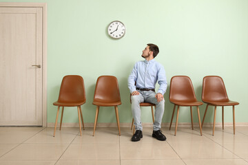 Young man looking at clock while waiting for job interview in room